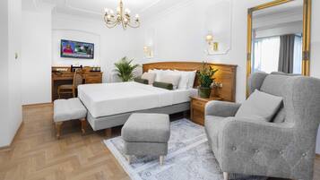 Een slaapkamer met een groot bed, een grijze fauteuil, een houten bureau en een televisie aan de muur.