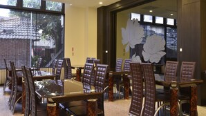 A conference room with a glass table surrounded by leather chairs with wooden bases, large windows with a view of trees, and a decorative wall with a floral design. - Midu Business Hotel (Xiluo)