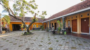 A courtyard with hexagonal paving, a tree, and a building with a tiled roof and yellow walls. - OYO 1721 A. Yani 95 Residence (Banyuwangi)