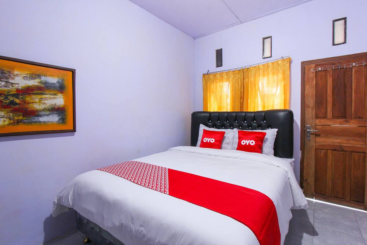 A bedroom with a bed, a wooden door, and a painting on the wall.
