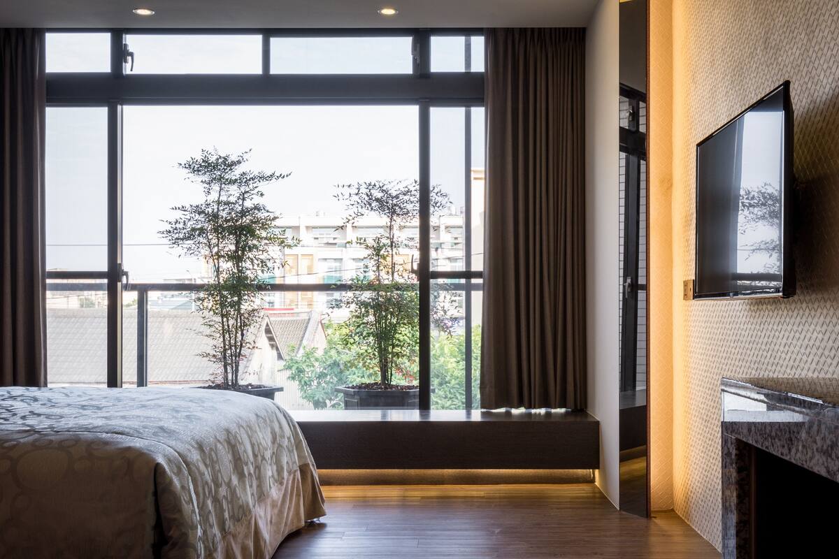 Une chambre d’hôtel avec une grande fenêtre, un lit, une télévision et une petite plante en pot.