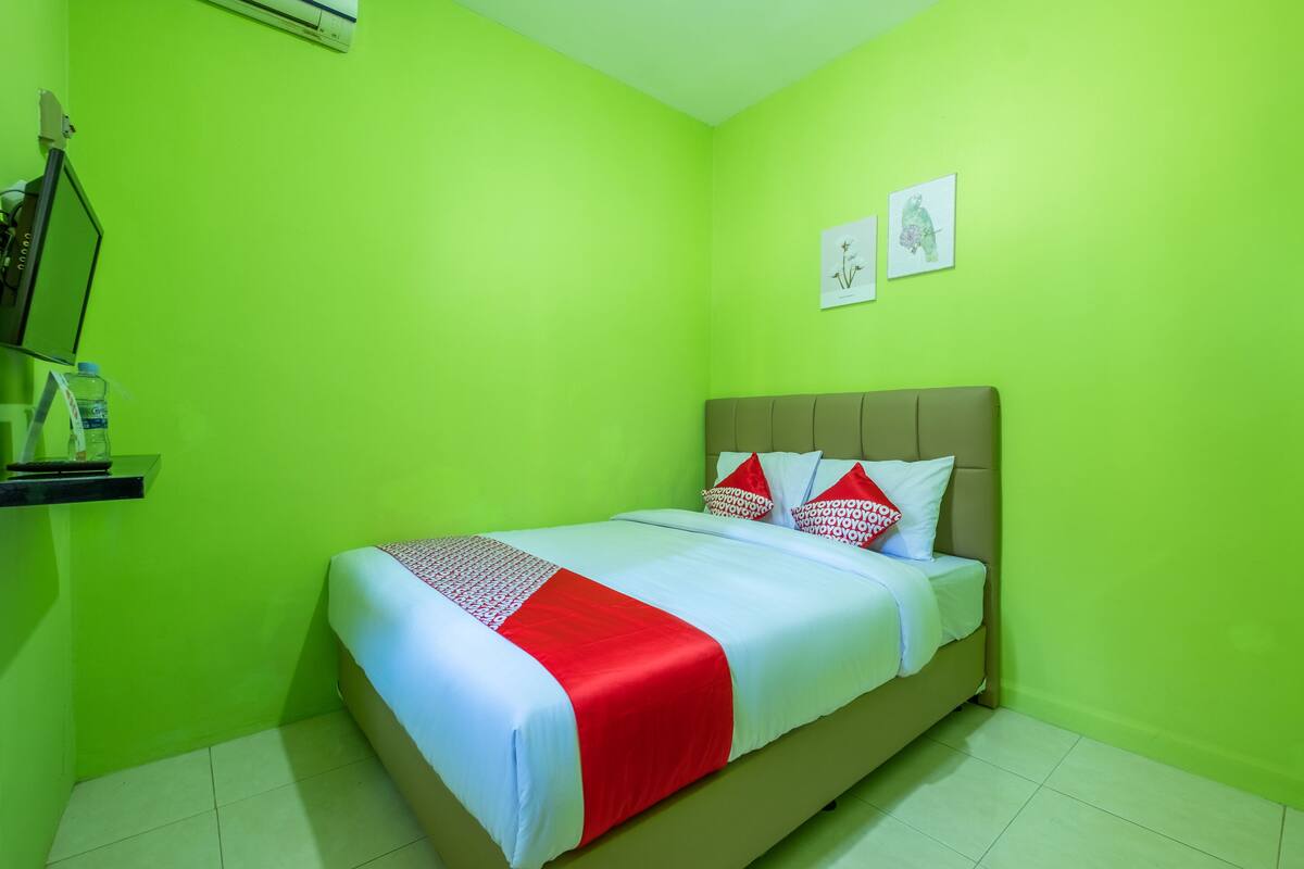 Une pièce avec un lit, des murs verts et deux tableaux encadrés accrochés au mur.
