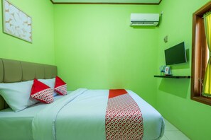 A room with a bed, a mounted TV, an air conditioner, and a window with curtains.