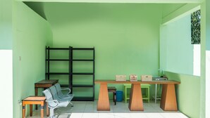 A room with a green wall, a wooden desk with a chair, a metal shelf unit, and a window with a view of trees. - OYO 1399 Cemara Residence Syariah (West Cirebon)