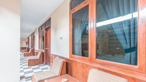 Un pasillo con ventanas de madera, suelo de cuadros y zonas de descanso con sillones acolchados y una pequeña mesa.