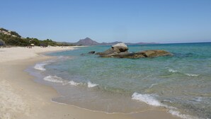 Ein Strand mit klarem türkisblauem Wasser, sandigem Ufer und Felsformationen.