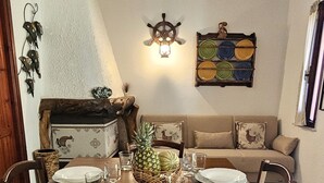 Ein Essbereich mit einem Holztisch, gedeckt für vier Personen, umgeben von Stühlen. Im Hintergrund sind eine hölzerne Kommode und ein Sofa zu sehen.
