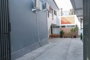 A courtyard with a grey wall, a metal gate, and a building with a red and white facade. There are potted plants and outdoor furniture. - Oyo 1454 111 Residence (Batu)