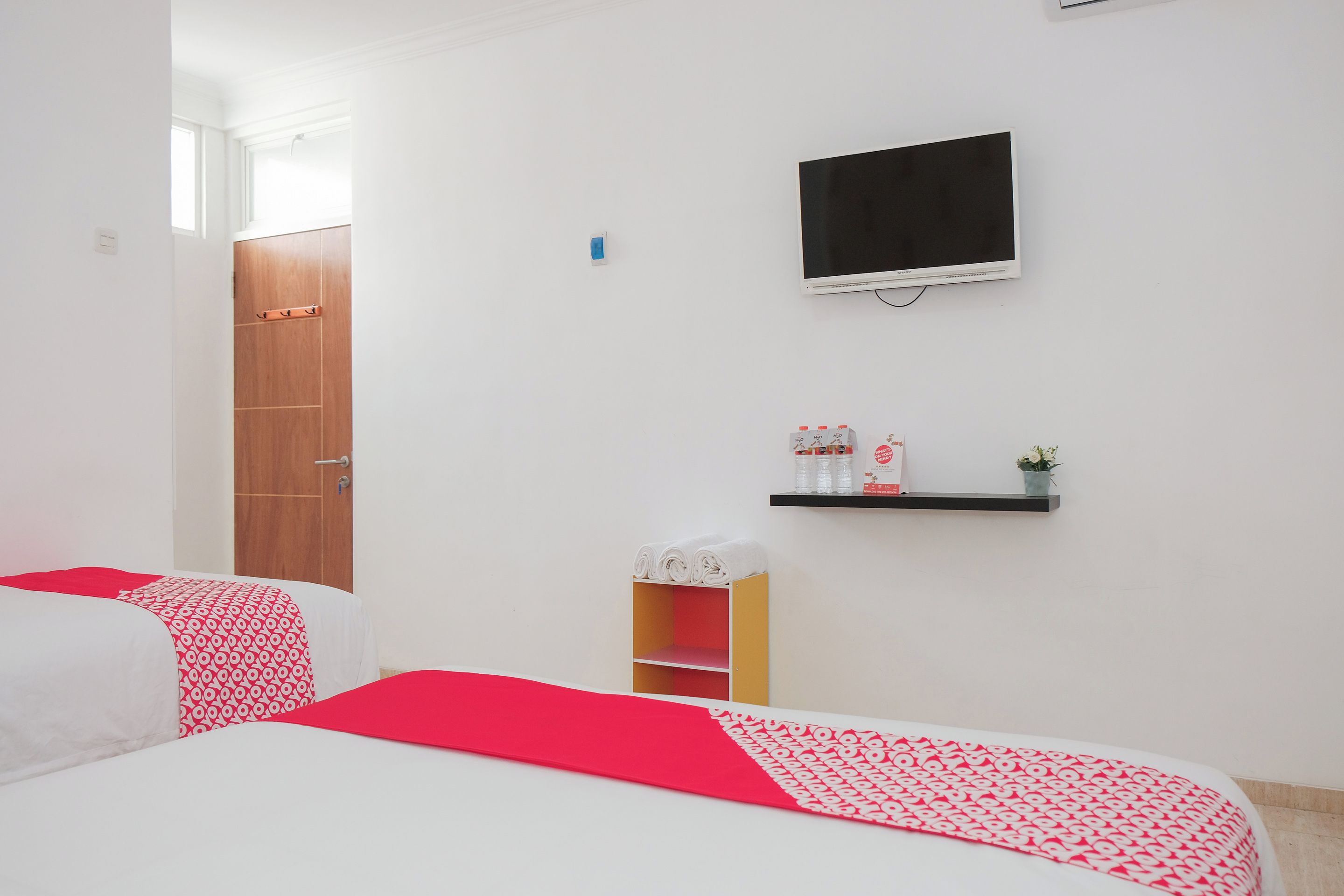 A bedroom with two beds, a TV, a shelf with toiletries, and a door.