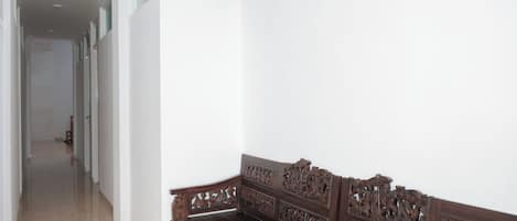 Een hal met een houten bank met ingewikkelde houtsnijwerken, een betegelde vloer en een witte muur met een raam.