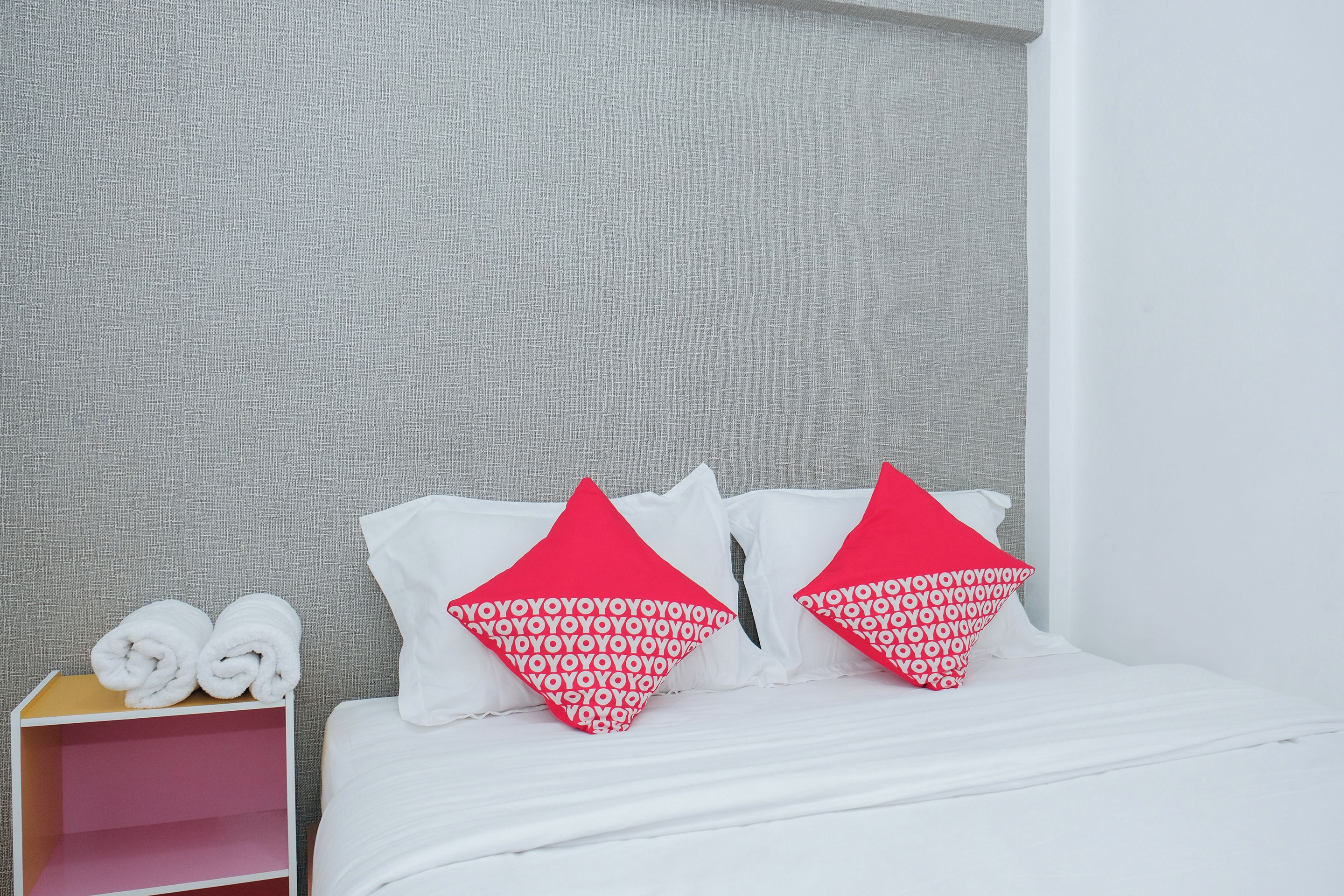 A hotel room with a bed, pillows, a nightstand, and a rolled-up towel.