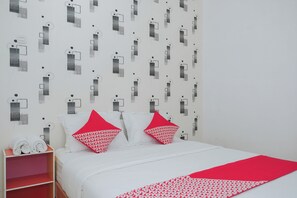 Un letto con lenzuola bianche e cuscini rossi, uno scaffale rosso con asciugamani e una parete decorata.