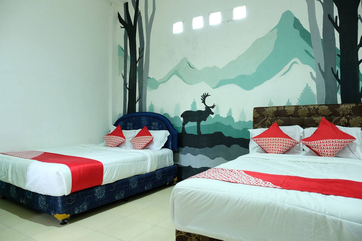 Dos camas individuales con ropa de cama roja y blanca, un mural con paisaje de montaña en la pared y suelo de baldosas.