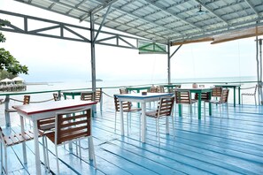 Un área de comedor al aire libre con mesas y sillas, un techo cubierto y vista al mar.