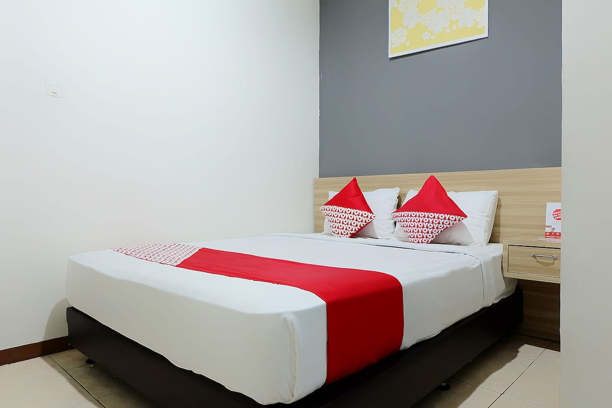 Una cama bien hecha con una colcha blanca y roja, un cabecero de madera y una mesita de noche con un cajón.