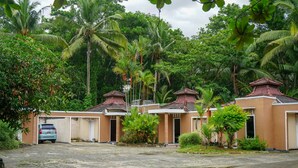 A row of two-story buildings with a uniform architectural style, surrounded by lush greenery and palm trees. - Hotel O Jatimas (Merawang)
