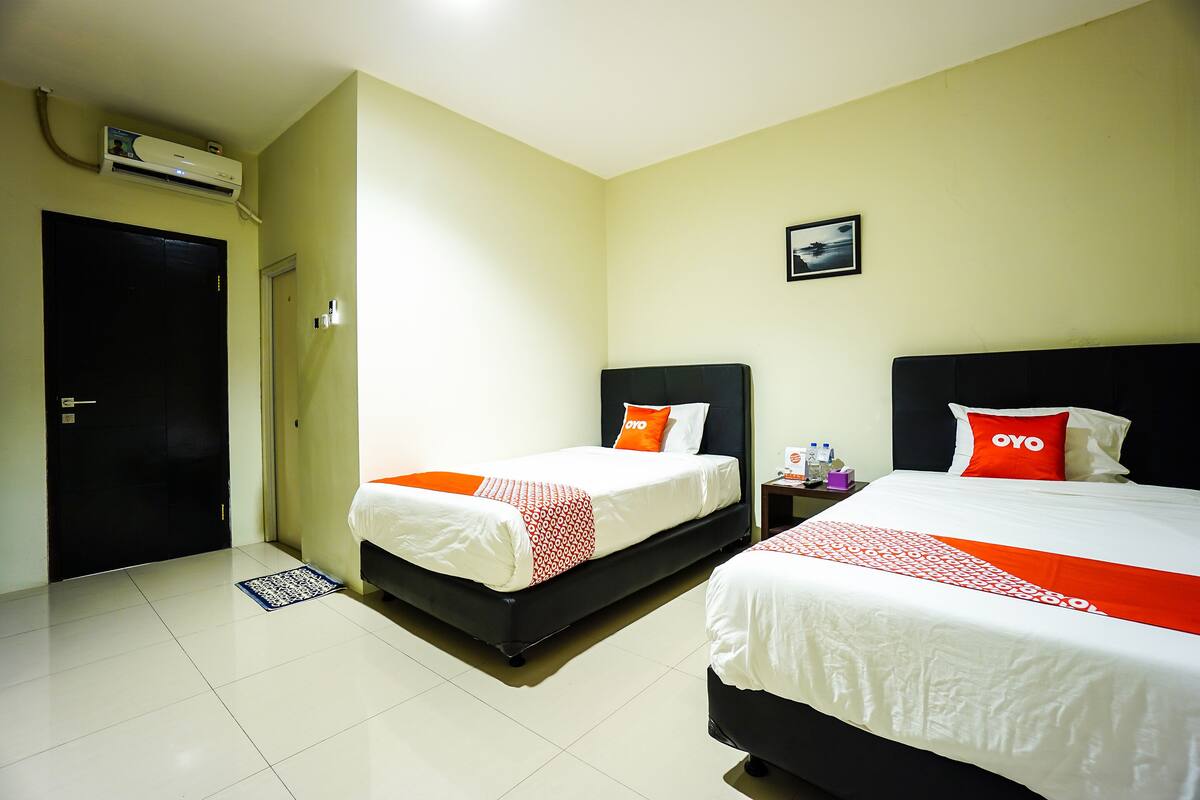 A hotel room with two beds, a black door, an air conditioning unit, and a small picture on the wall.