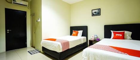 A hotel room with two beds, a black door, an air conditioning unit, and a small picture on the wall.