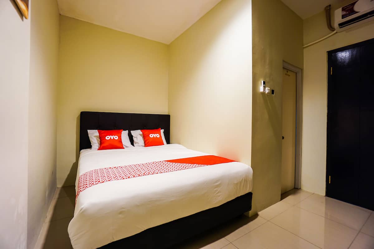 A hotel room with a bed, a black headboard, and a door.
