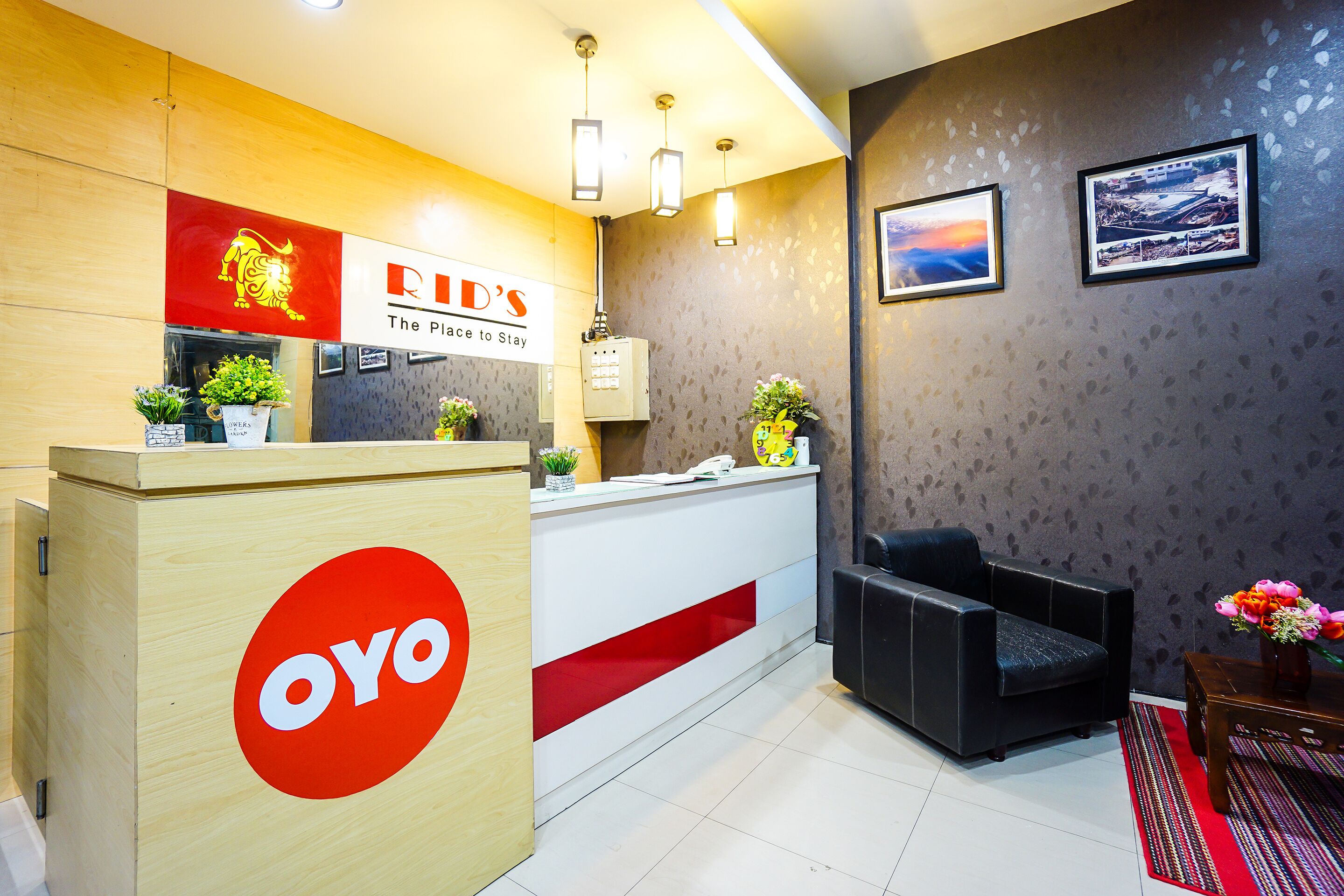 A hotel reception area with a wooden reception desk, a black leather sofa, and a red and white sign that reads "RID'S The Place to Stay."
