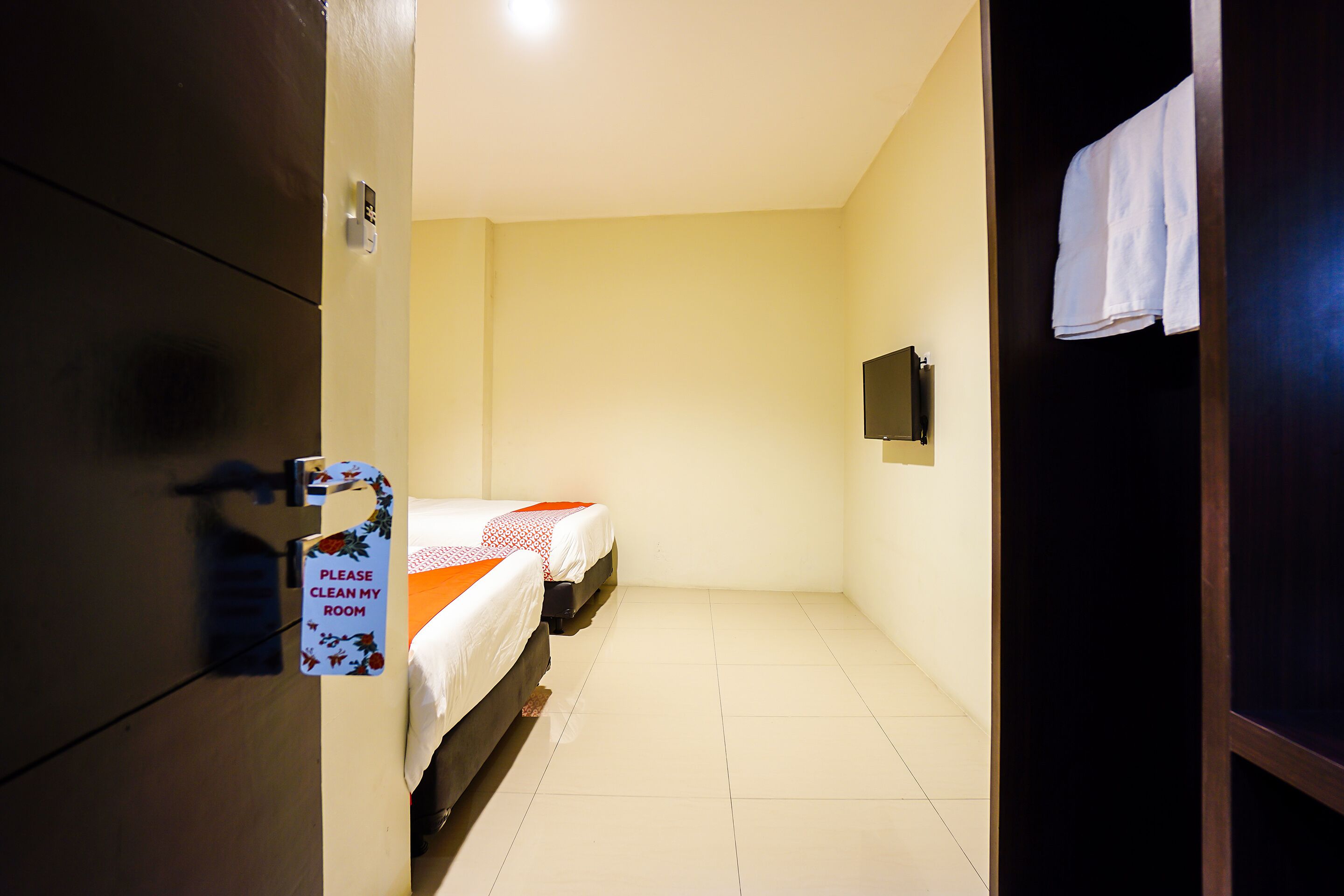 A hotel room with a bed, a small TV, and a sign requesting guests to clean the room.