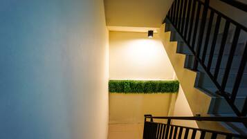 A staircase with a black railing, a light fixture on the wall, and a green plant decoration.