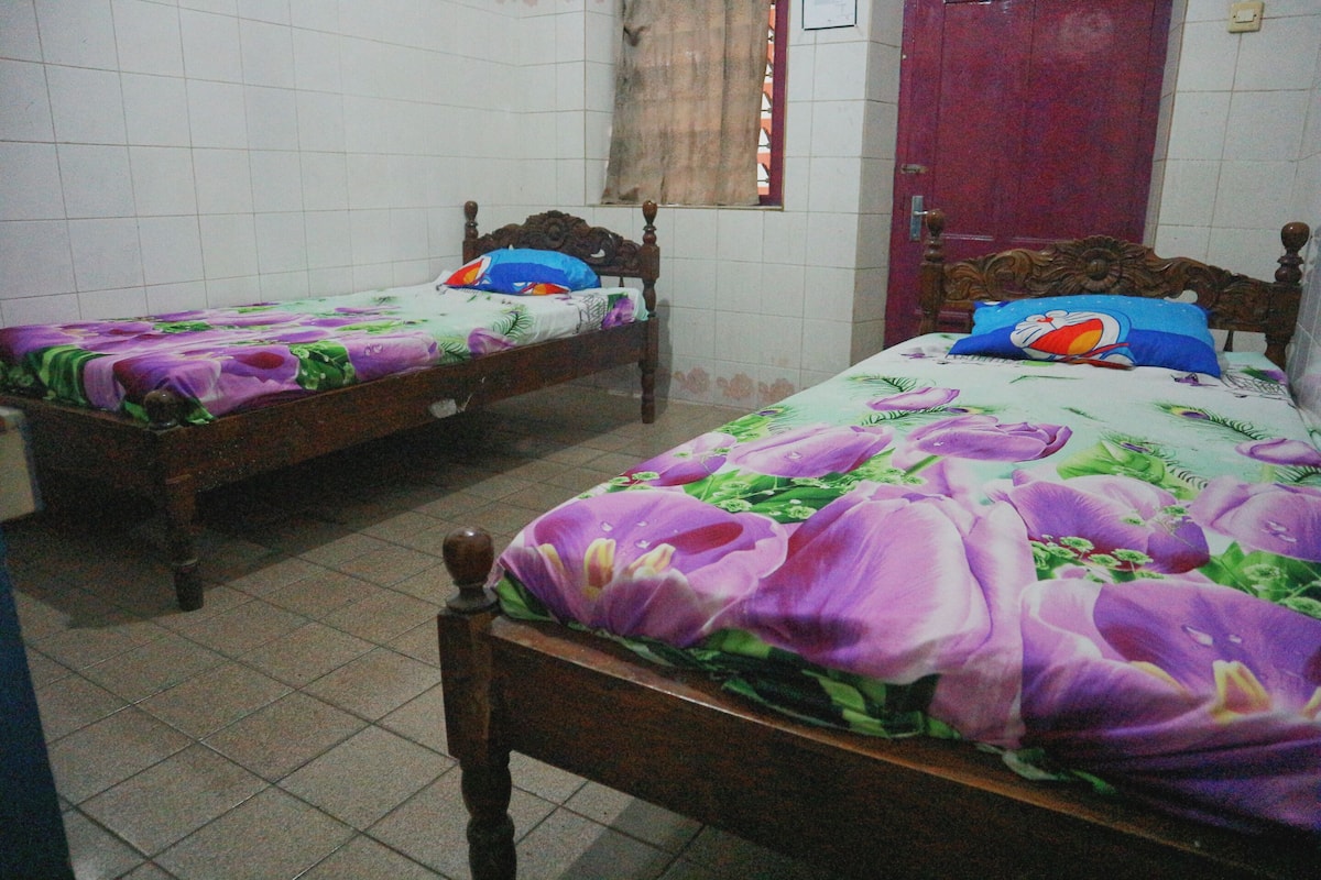 Two wooden beds with floral bedding, a tiled floor, and a red door.