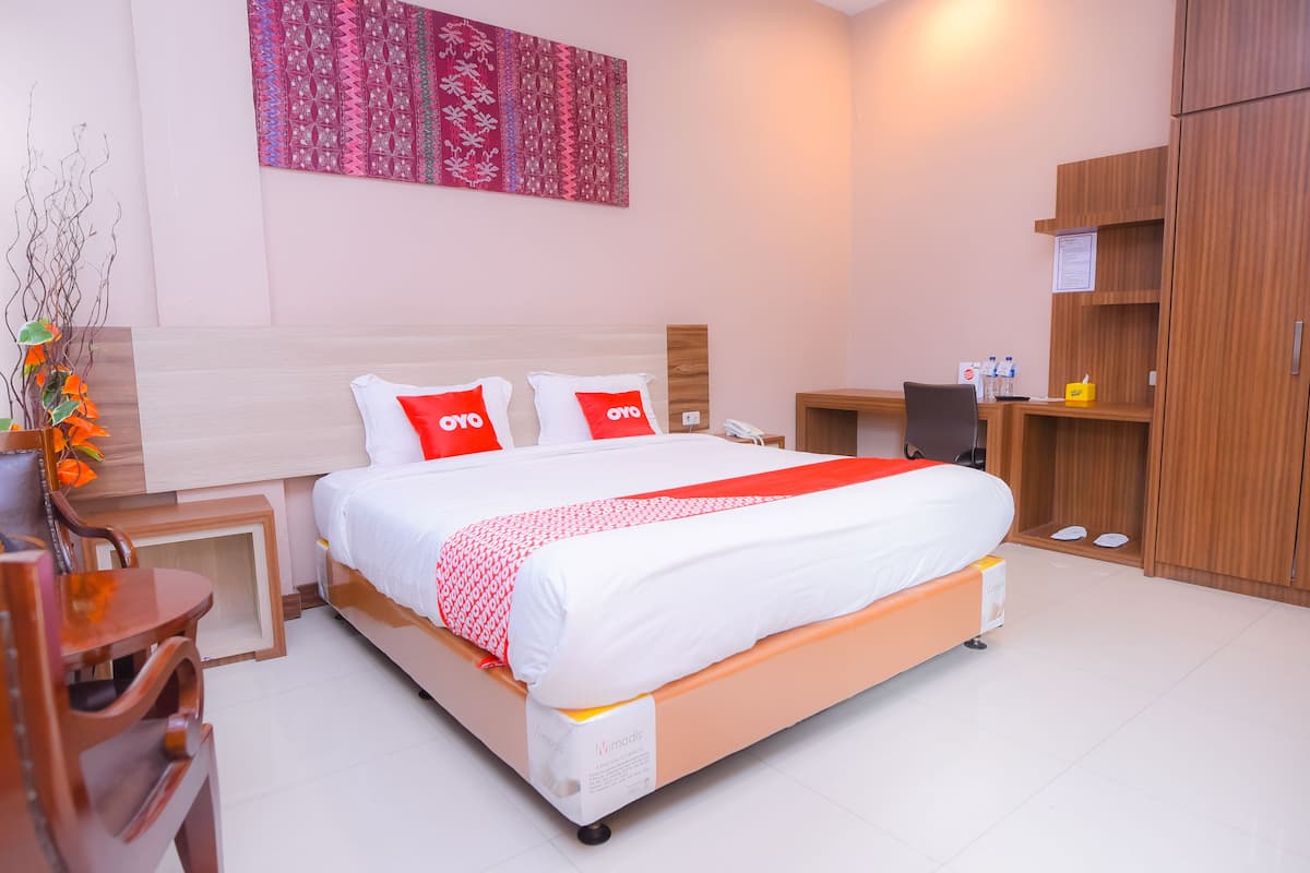 Een moderne hotelkamer met een opgemaakt bed, een houten nachtkastje, een bureau met stoel, een kledingkast en een decoratief wandobject.
