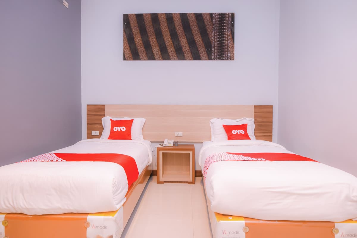Een tweepersoonskamer met twee bedden, elk voorzien van witte beddengoed en rode accenten, een houten hoofdbord en een klein nachtkastje met een telefoon.