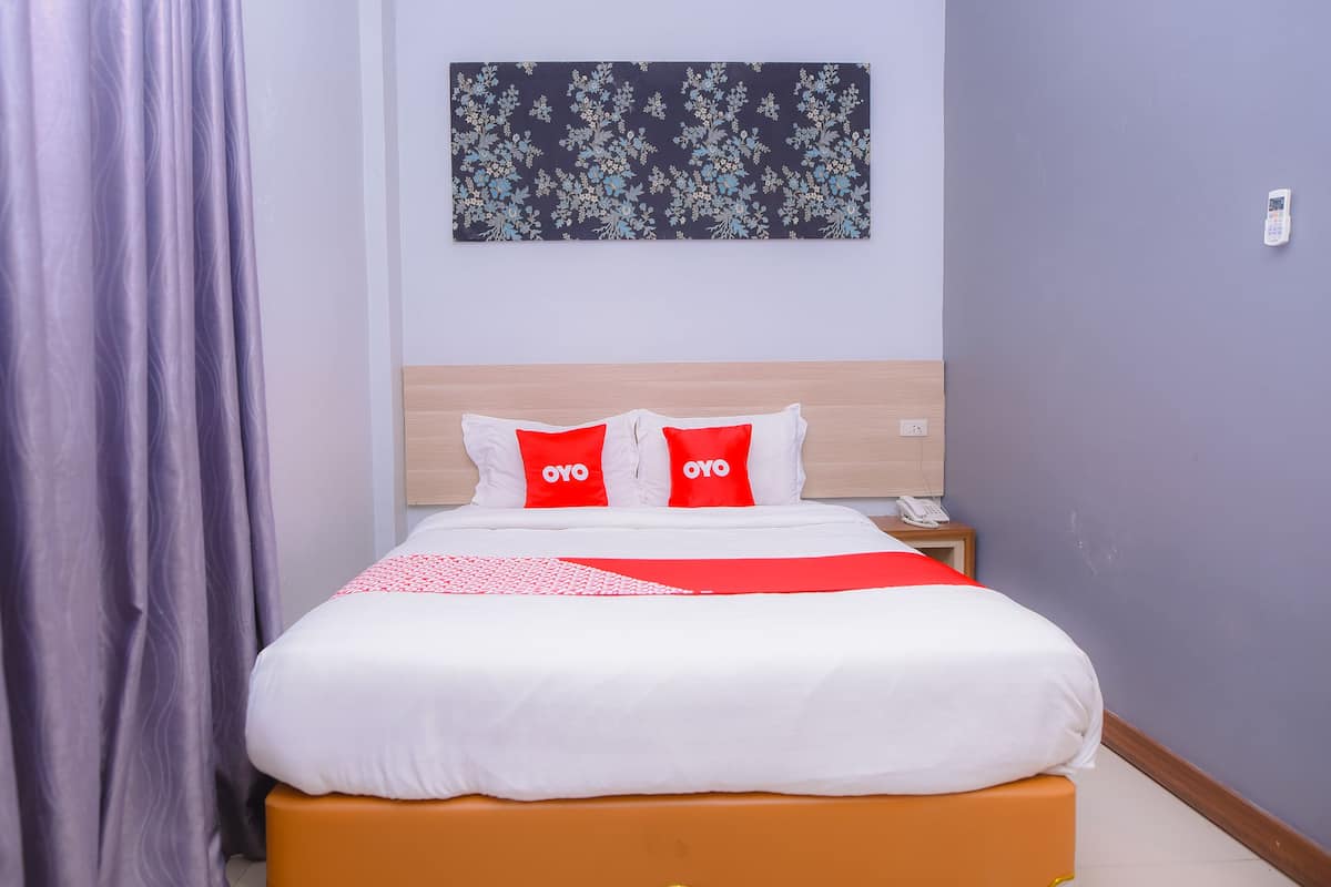 Een opgemaakt bed met wit en rood beddengoed, een houten hoofdbord en een bloemig kunstwerk aan de muur.