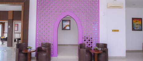 Un área de recepción con un separador decorativo morado, dos sillones de cuero marrón y una mesita con un jarrón.