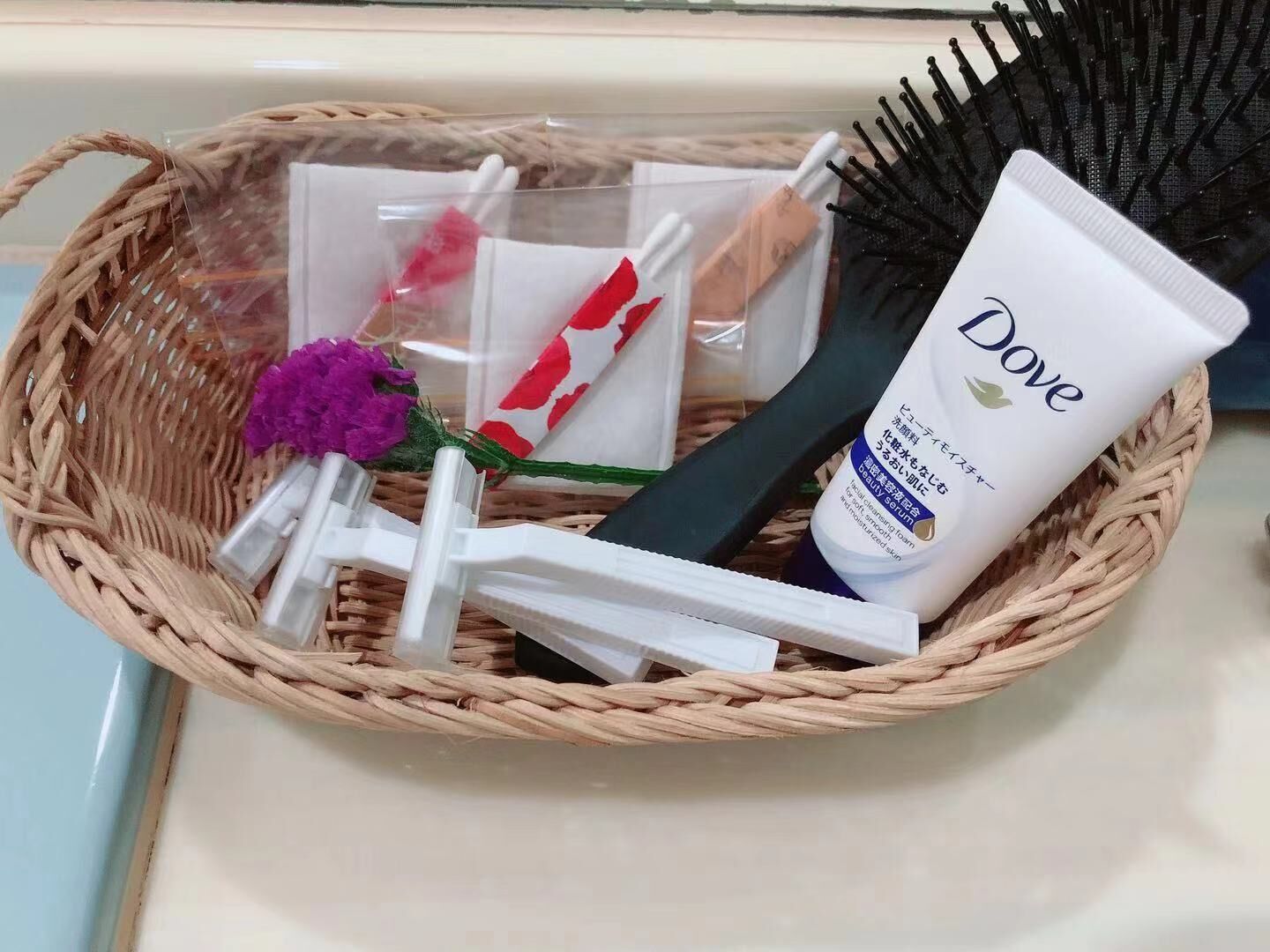 A wicker basket containing Dove skincare products, a hairbrush, and a purple flower.