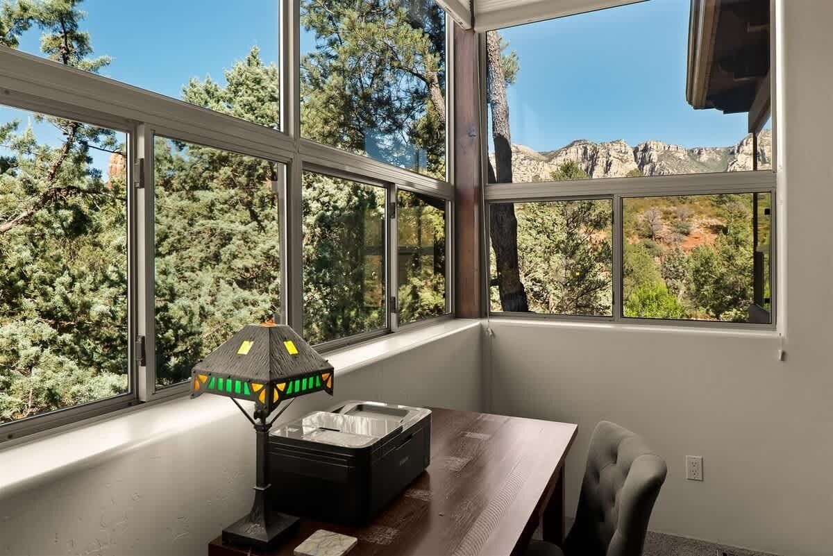 A room with large windows, a small table, a chair, and a decorative lamp.