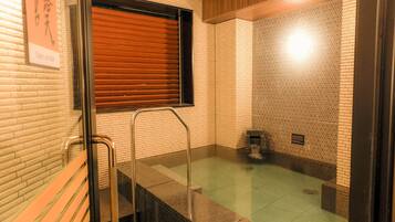 A modern bathroom with a glass shower enclosure, a wooden bench, and a tiled wall with a geometric pattern.