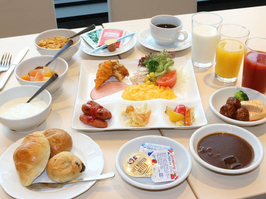 Una mesa de desayuno con diversos platos, incluyendo huevos, salchichas y bollería.