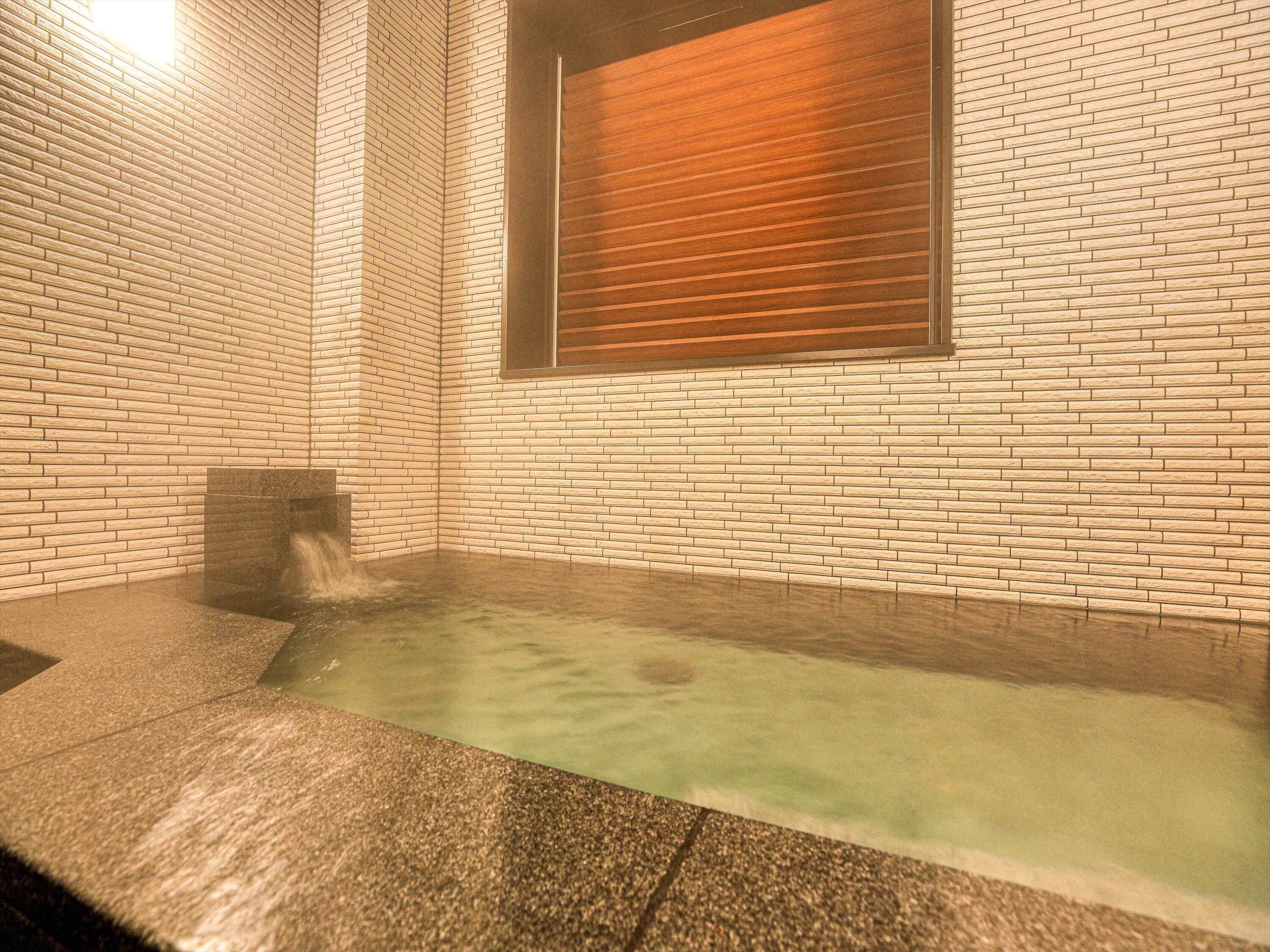 A spa area with a hot tub, tiled walls, and a window with blinds.