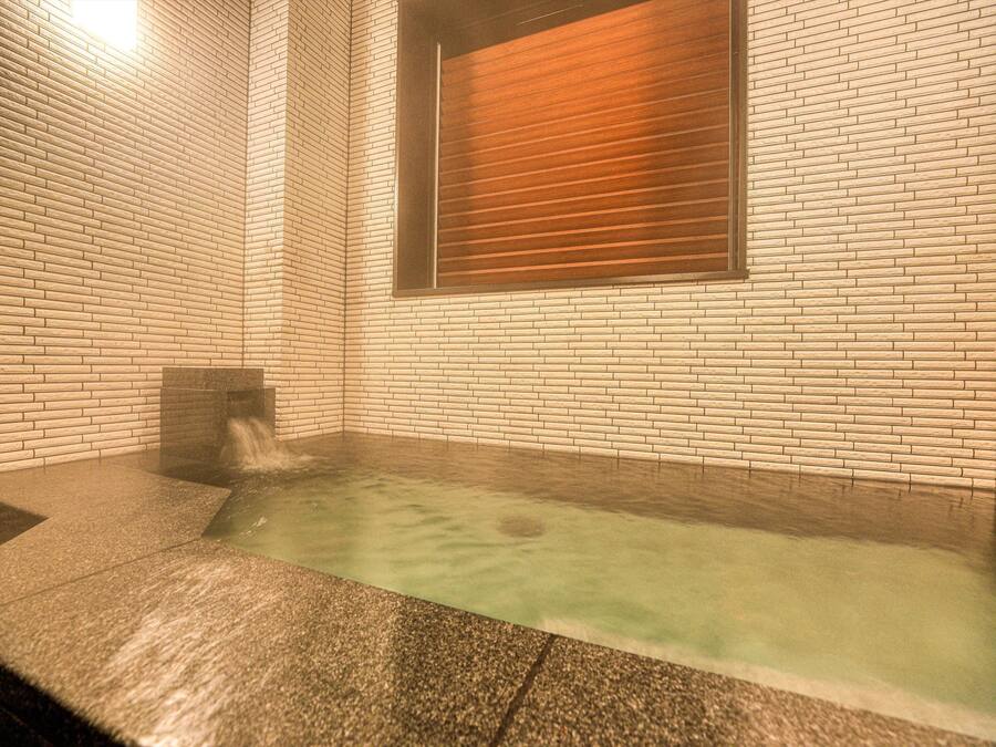 A spa area with a hot tub, tiled walls, and a window with blinds.