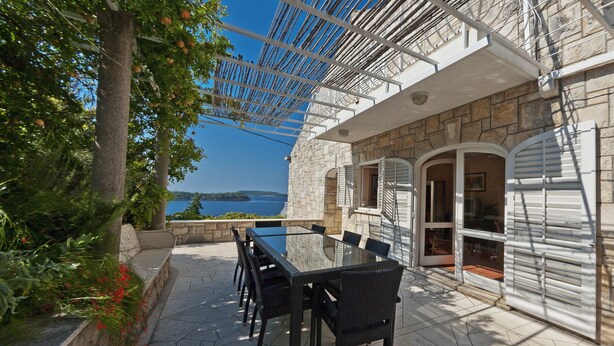 Une terrasse extérieure avec une table et des chaises, un mur en pierre et une vue sur la mer.
