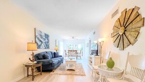 A spacious living room with a blue sofa, a coffee table, and a dining area with white chairs. - Siesta Key Beachfront Escape 3 BR Condo (Siesta Key)