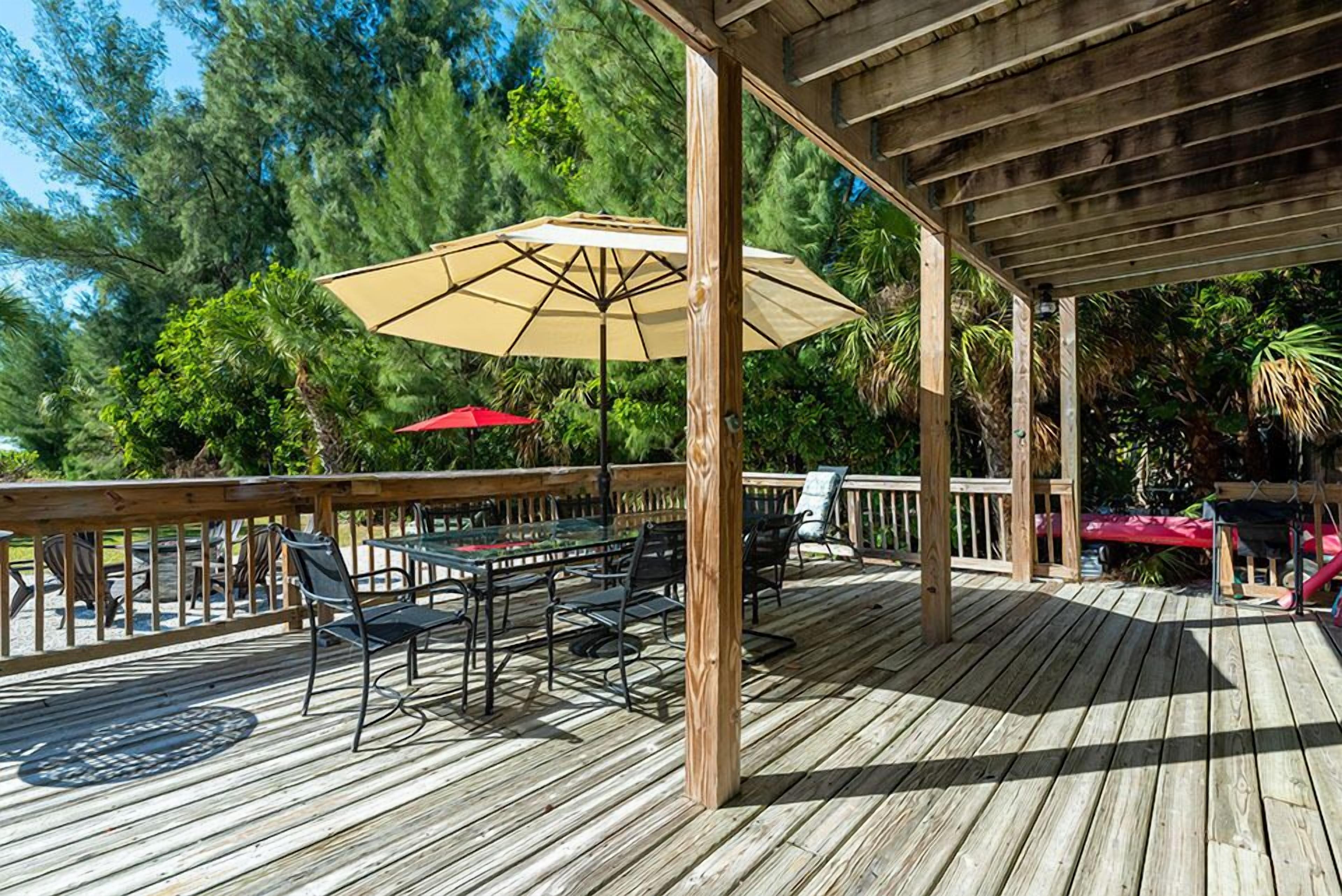 An outdoor deck with wooden flooring, a table with chairs, and two umbrellas.