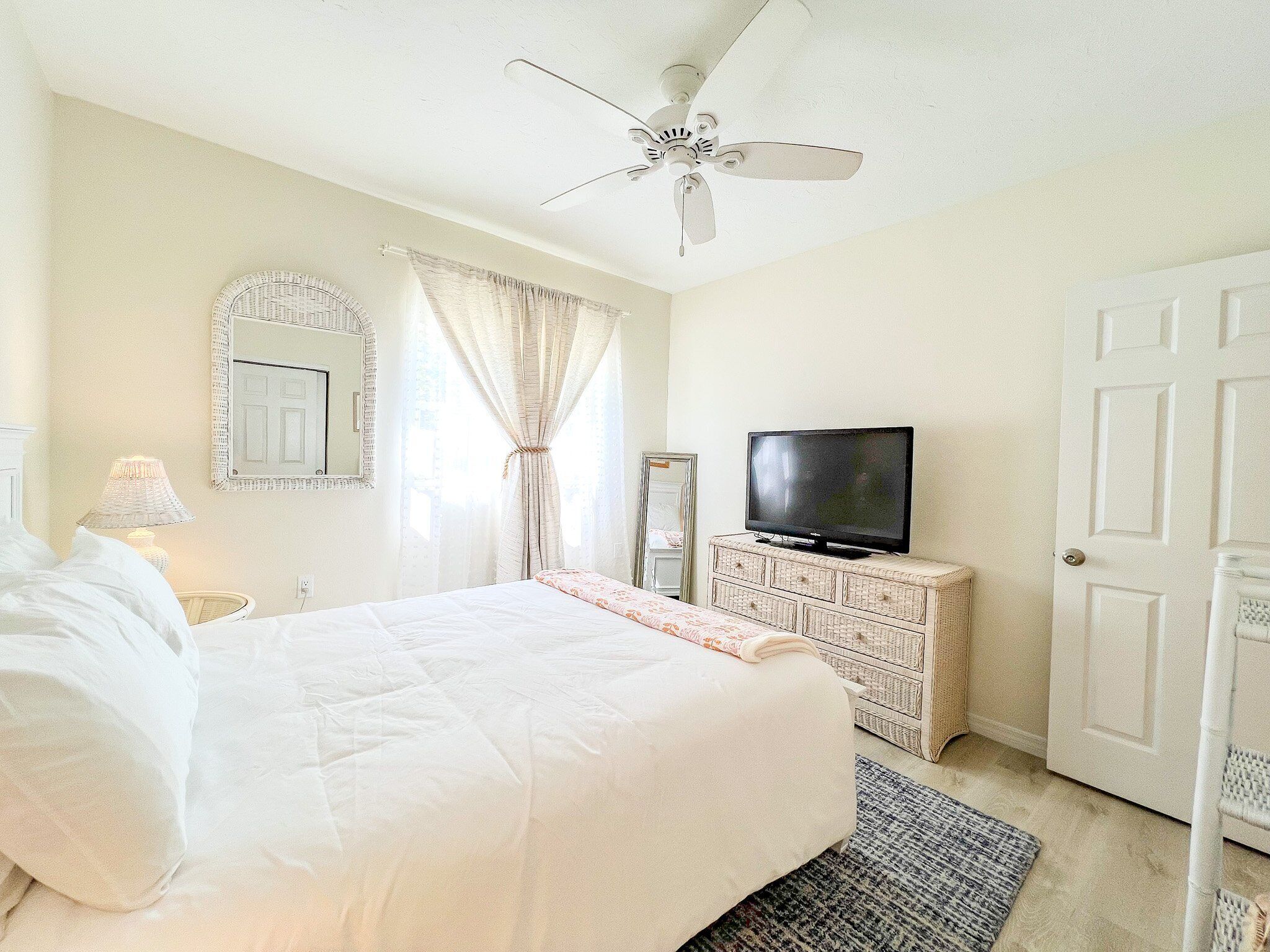Une chambre à coucher avec un lit, un téléviseur posé sur une commode, un ventilateur de plafond et une porte.