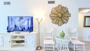 Een woonkamer met een televisie waarop een vakantiehuis staat afgebeeld, witte meubels en een decoratief kunstwerk aan de muur.