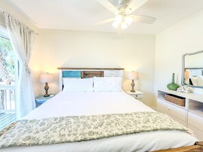 A bedroom with a bed, a nightstand, a lamp, a ceiling fan, a window with curtains, and a mirror on the wall. - Siesta Key Beachfront Escape 3 BR Condo (Siesta Key)