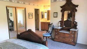 A bedroom with a bed, dresser, mirror, chair, and a door leading to another room.
