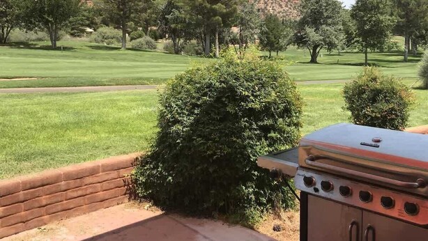 A patio with a grill, a brick wall, and a view of a golf course and mountains.