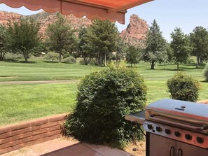 A patio with a grill, a brick wall, and a view of a golf course and mountains.
