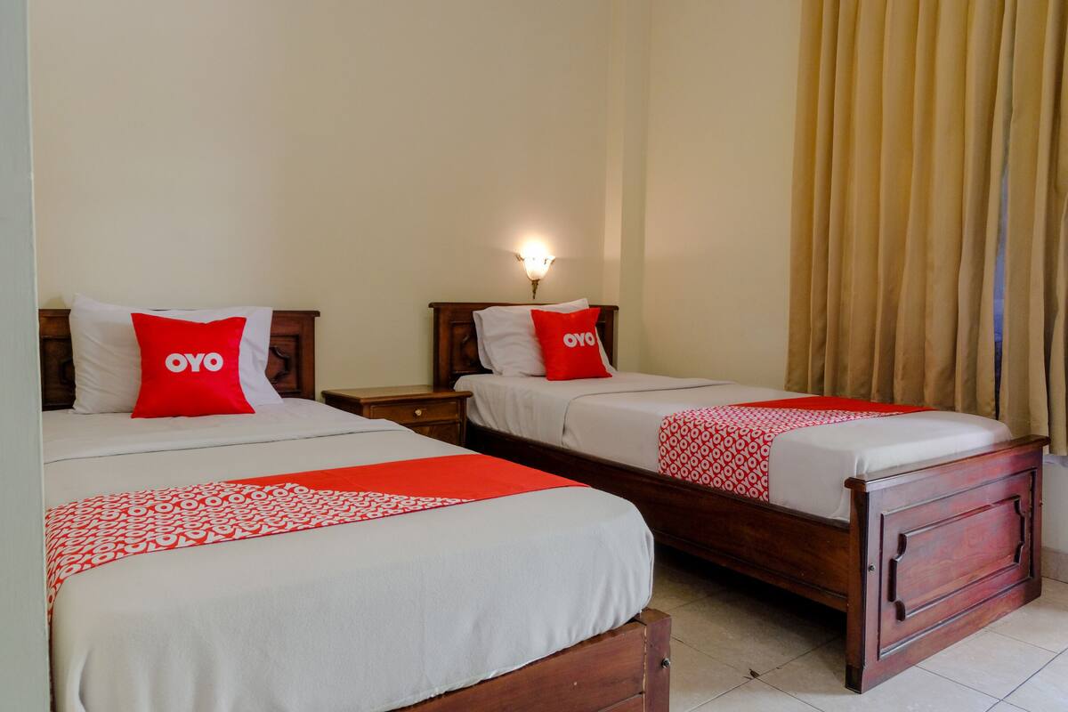 Habitació d'hotel amb dos llits, cadascun amb un coixí vermell d'OYO i un llençol amb estampat.
