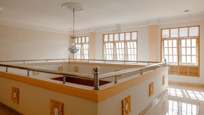 Ein großzügiger Innenbereich mit einem großen, rechteckigen Pool, Deckenventilator und großen Fenstern mit Holzläden.
