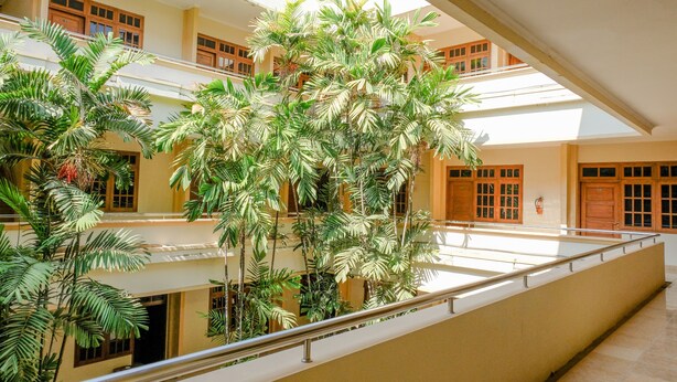 Ein mehrgeschossiges Atrium mit einer zentralen Treppe, umgeben von üppiger Vegetation und mehreren Balkonen.