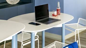 Une pièce moderne avec une table blanche, un ordinateur portable, un téléphone intelligent, une bouteille et un bol posés sur une étagère.